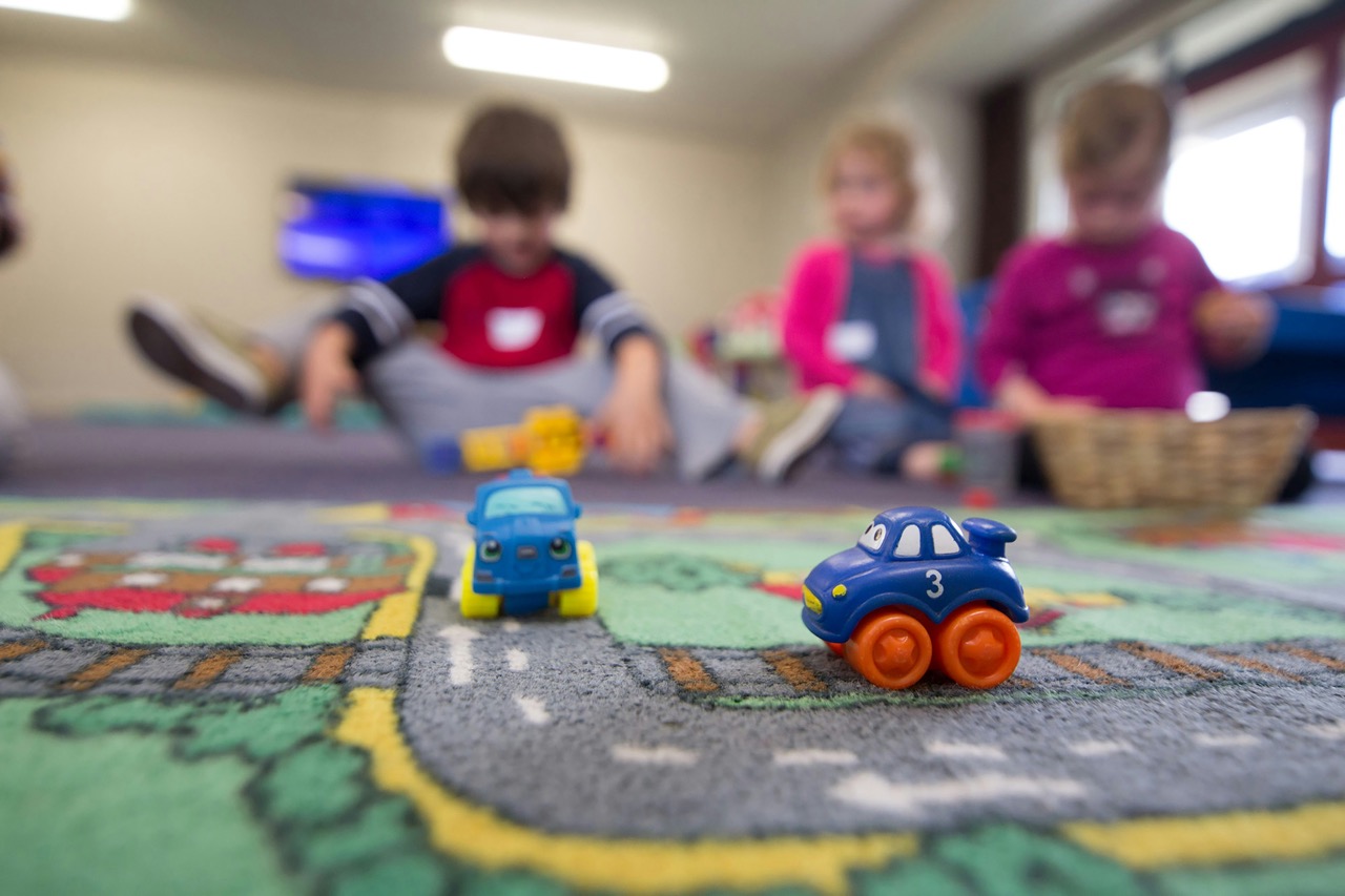Children playing with small toy cars on a classroom road rug