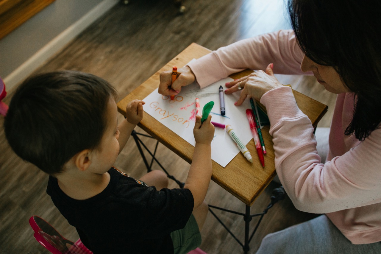 A teacher helping a young child with a coloring activity at a small table