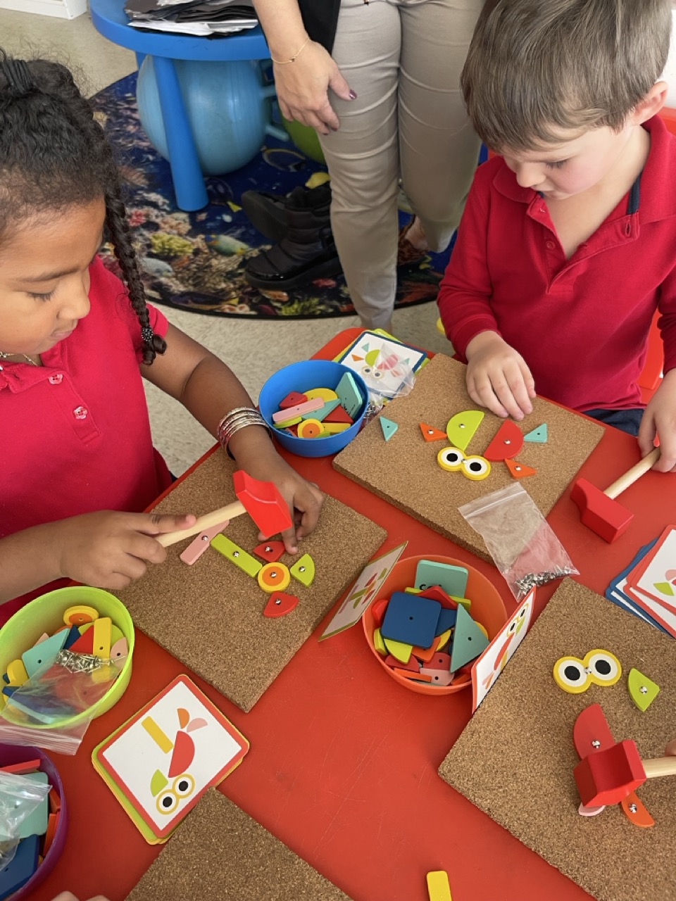 Niños de preescolar siguiendo tarjetas ilustradas para crear manualidades de formas durante una actividad práctica