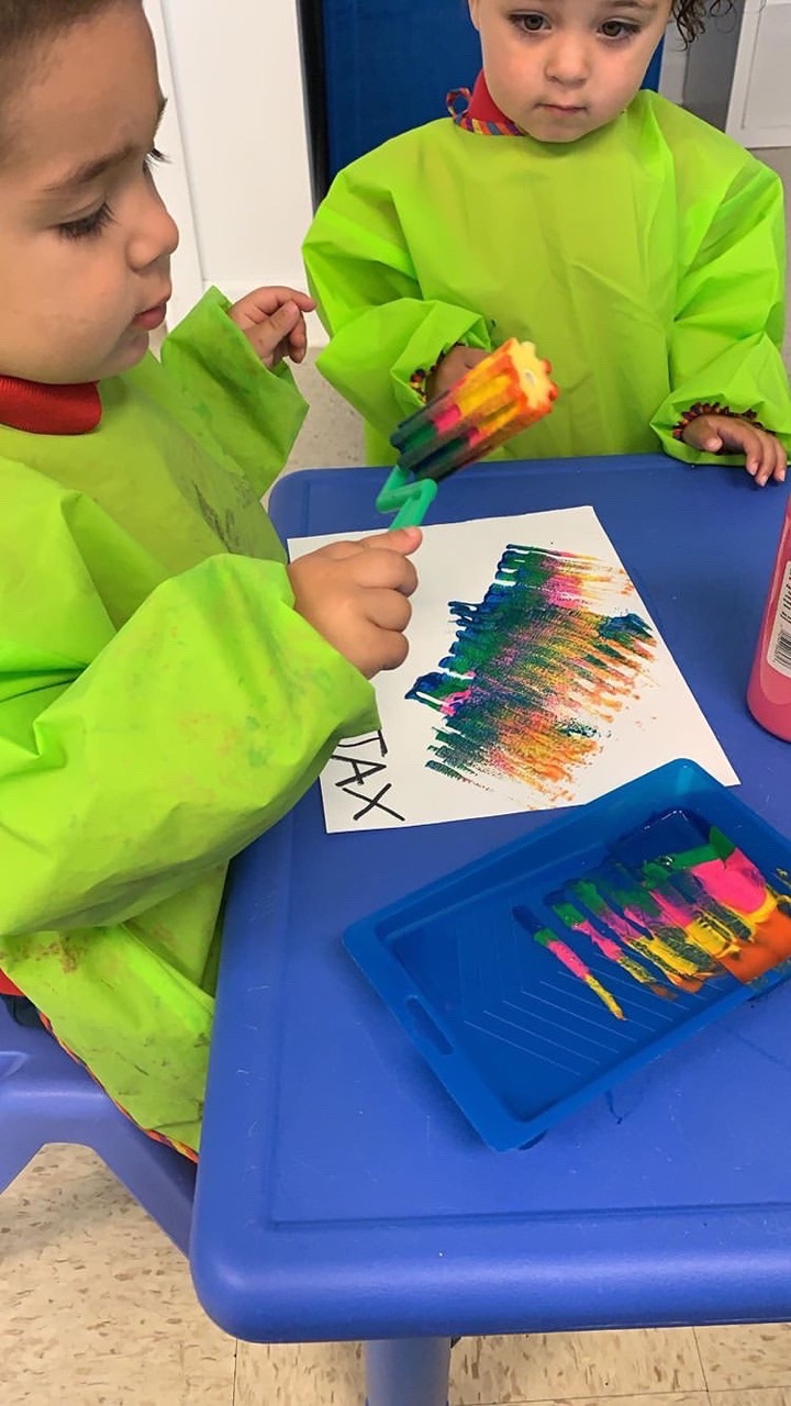 Niños pequeños con batas de arte pintando juntos en la mesa de actividades de Malave Child Care Center