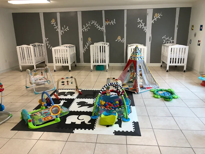 The infant room at Malave Child Care Center with cribs and a soft play-mat area for tummy time and exploration