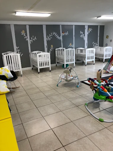 Infant nap area with cribs and a hand-painted tree mural