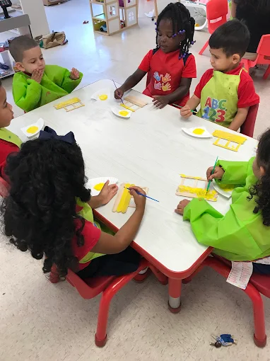 Preschool-age children doing a hands-on painting activity together at a classroom table
